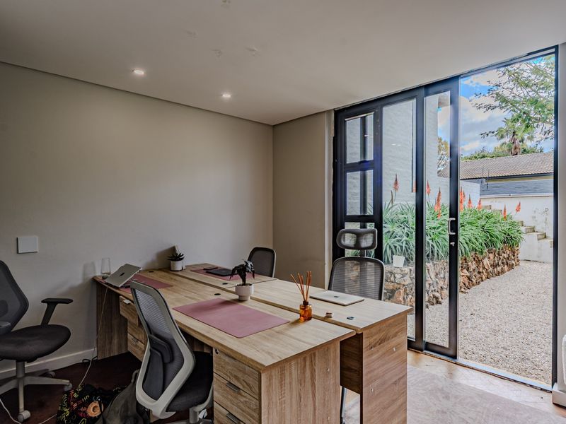 A bright home office featuring recessed lighting and large aluminium sliding doors that open directly onto a landscaped garden area.