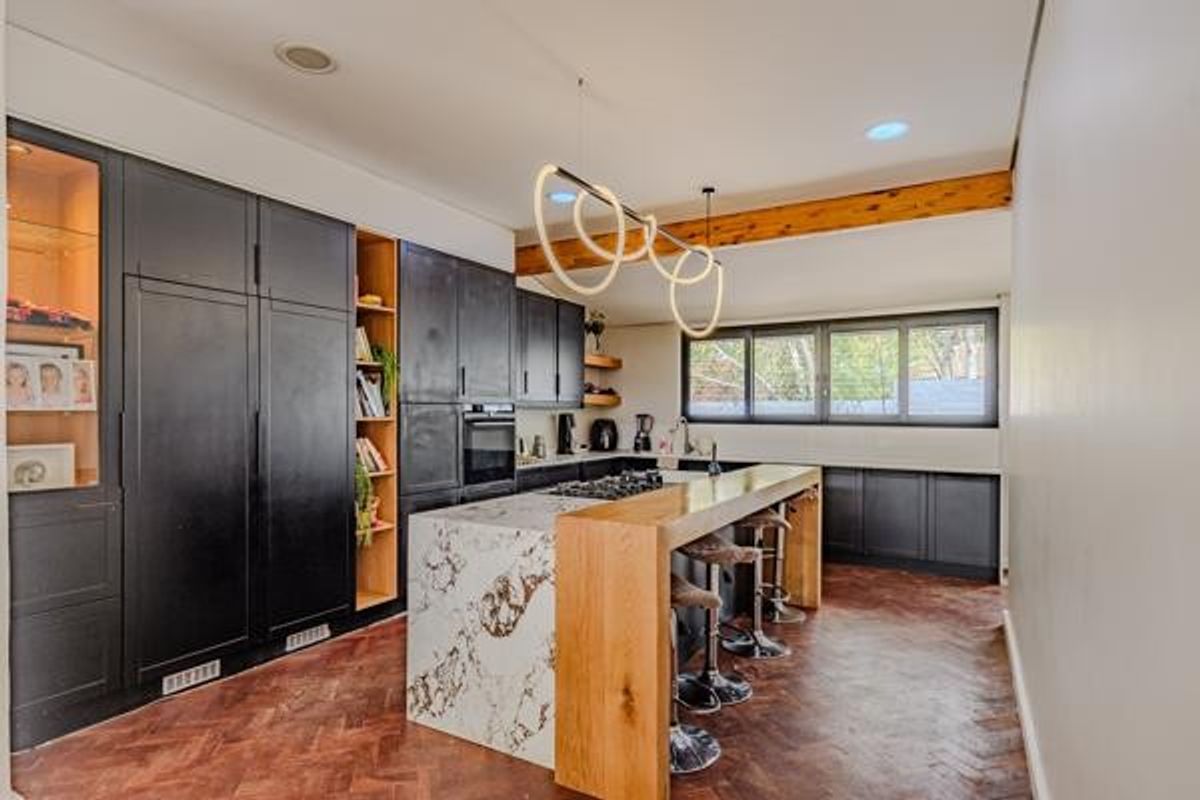 Modern kitchen featuring dark cabinetry, a marble-topped island with a wooden breakfast bar, herringbone timber flooring, and an exposed ceiling beam.