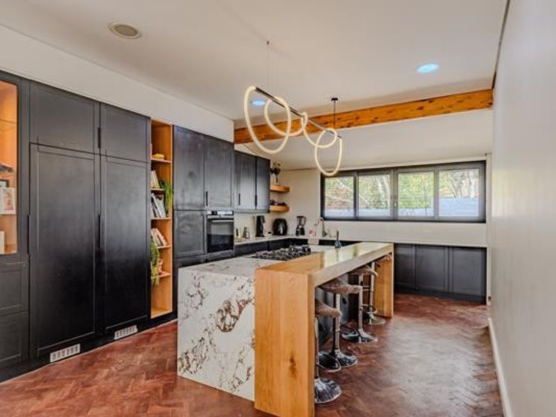 Modern kitchen featuring dark cabinetry, a marble-topped island with a wooden breakfast bar, herringbone timber flooring, and an exposed ceiling beam.