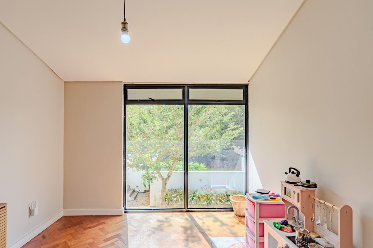 A bright bedroom featuring classic herringbone parquet flooring and a large black-framed sliding glass door providing natural light and garden views.