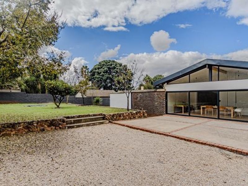 Rear view of the property featuring a modern extension with large sliding glass doors, a concrete patio, and a landscaped garden with stone retaining walls.
