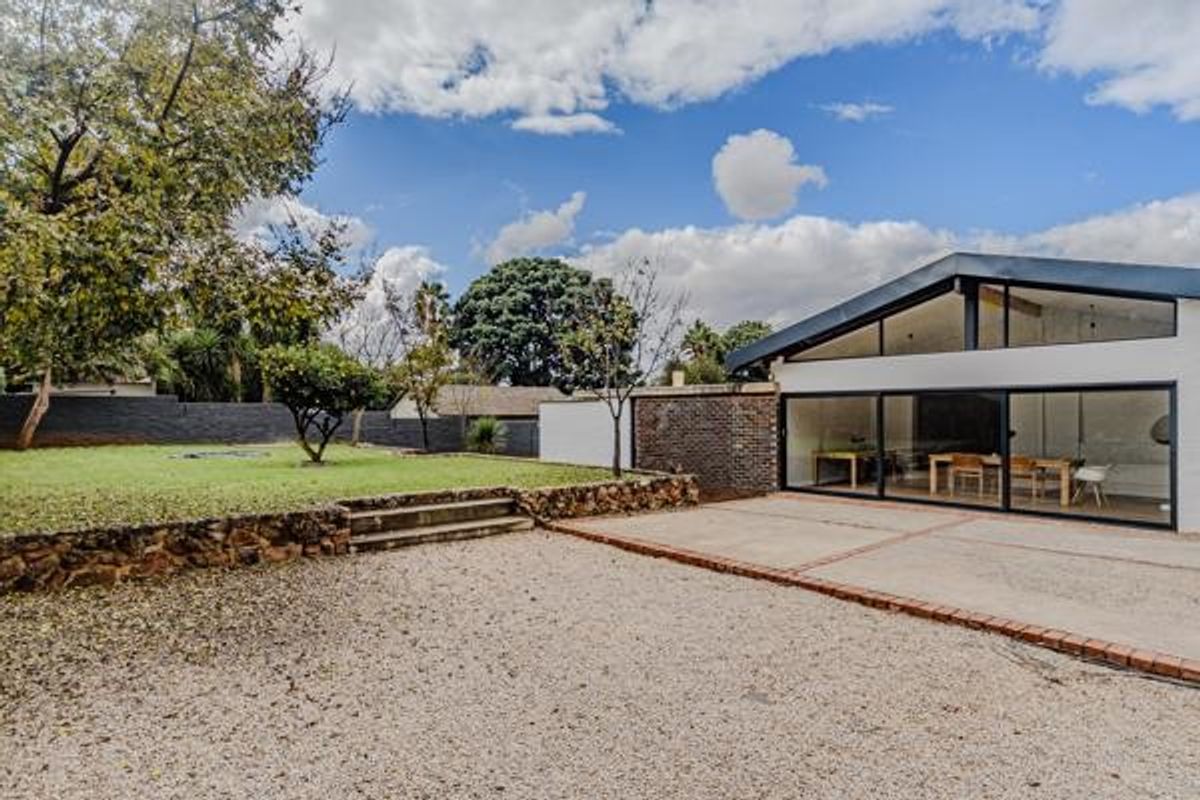 Rear view of the property featuring a modern extension with large sliding glass doors, a concrete patio, and a landscaped garden with stone retaining walls.