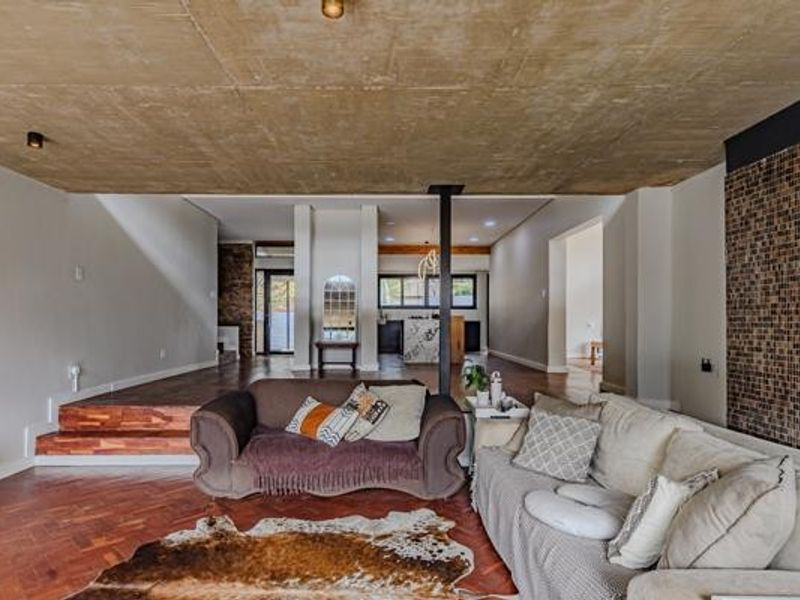 Spacious open-plan living area featuring a unique exposed concrete ceiling, warm parquet flooring, and a striking mosaic tile feature wall.