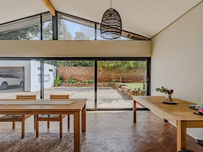 Spacious open-plan living area featuring vaulted ceilings, clerestory windows, and large sliding glass doors that open onto a paved rear patio and garden.