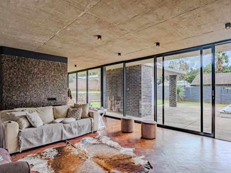 Spacious living area featuring an exposed concrete ceiling, herringbone parquet flooring, a textured stone feature wall, and large sliding glass doors opening to the patio.