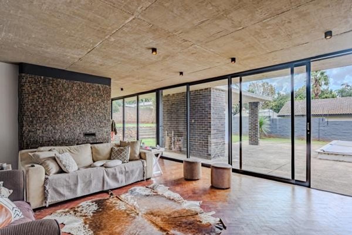 Spacious living area featuring an exposed concrete ceiling, herringbone parquet flooring, a textured stone feature wall, and large sliding glass doors opening to the patio.