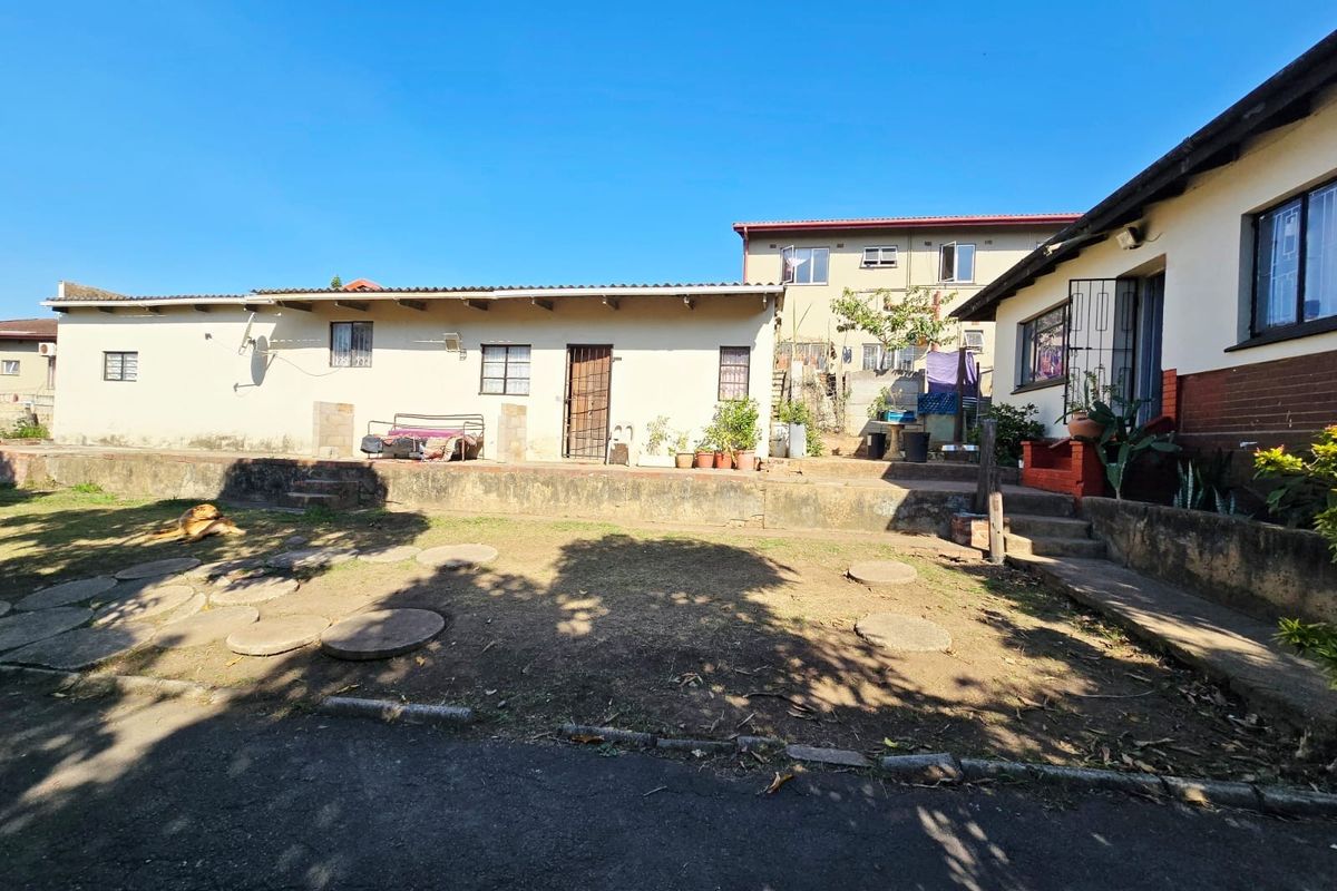 Rear exterior view of the property featuring a paved patio area, concrete retaining wall, and access to the main dwelling and outbuilding.
