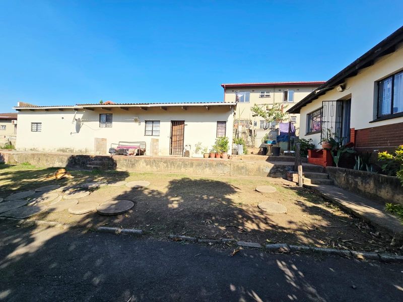 Rear exterior view of the property featuring a paved patio area, concrete retaining wall, and access to the main dwelling and outbuilding.