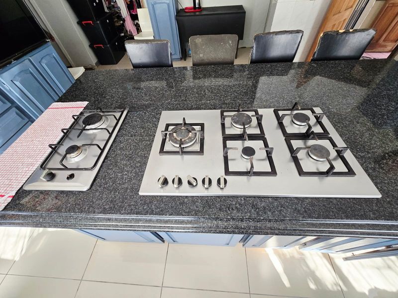 Kitchen island featuring a large granite countertop with integrated dual gas hobs and built-in cabinetry underneath.
