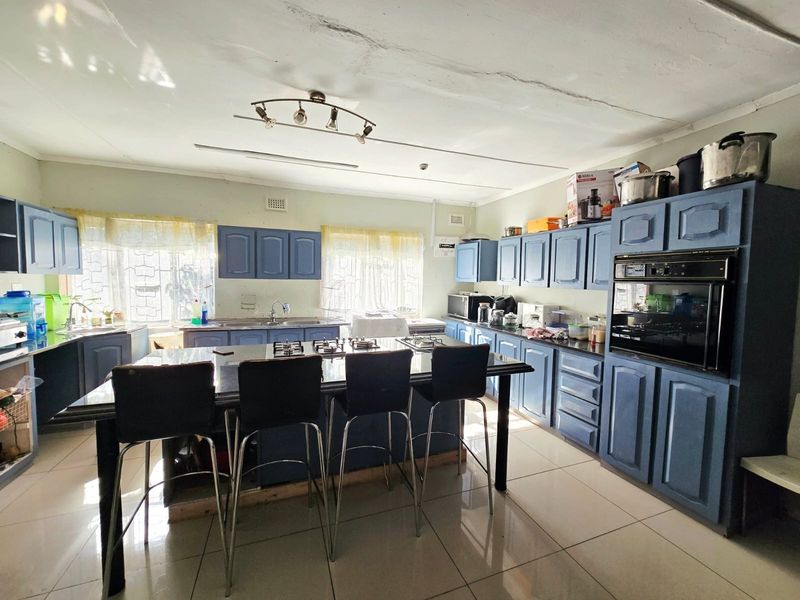 Spacious kitchen featuring blue cabinetry, a central island with a built-in gas hob, integrated oven, and tiled flooring throughout.