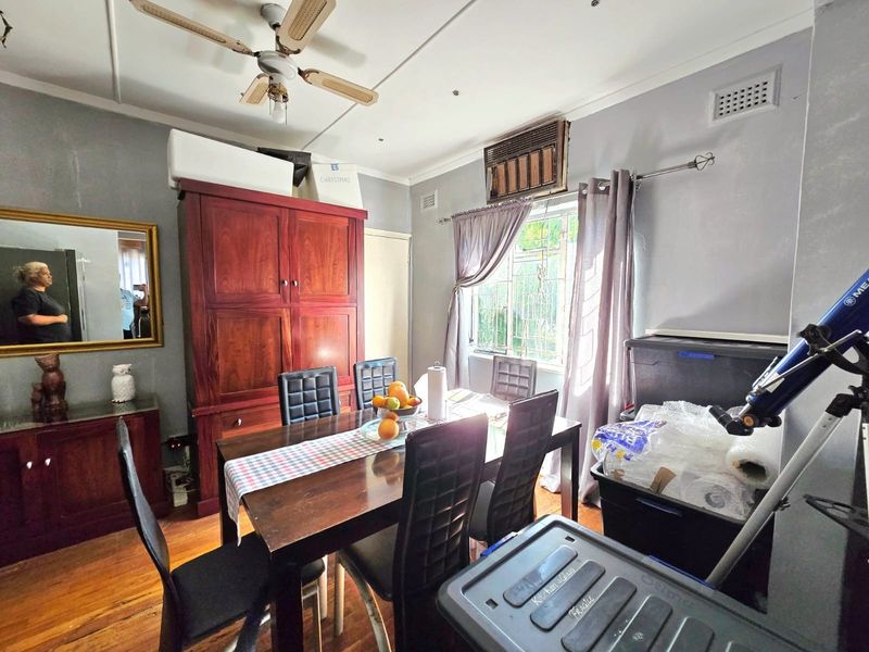 A dining room featuring timber flooring, a ceiling fan, and a wall-mounted air conditioning unit, providing a functional space for meals.
