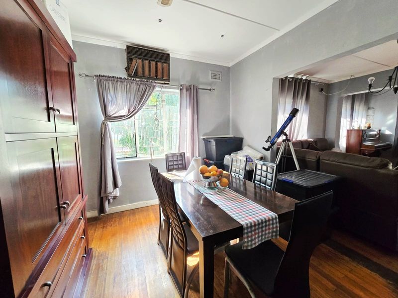 A dining area featuring timber flooring and an integrated window air conditioning unit, flowing into an adjacent living space.