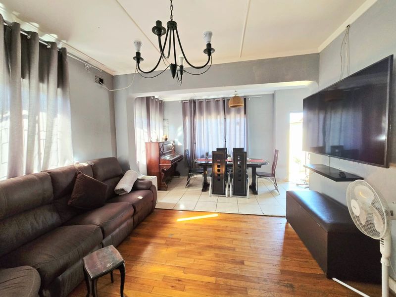 An open-plan living and dining area featuring polished wooden flooring, tiled dining section, and a central chandelier, creating a functional and connected living space.