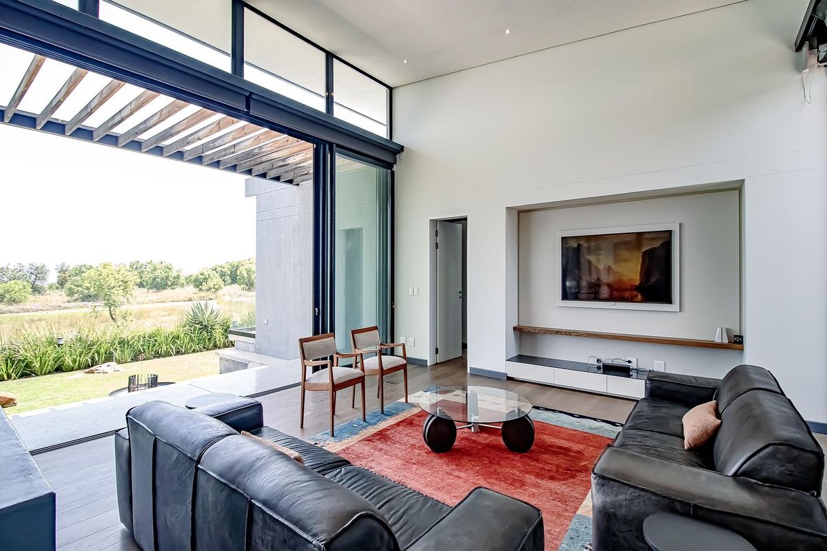 Modern living room featuring high ceilings, large sliding glass doors opening to a patio, and a custom recessed media wall with timber shelving.