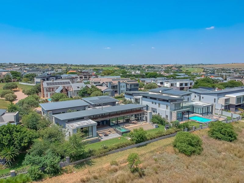 Aerial view of a modern residential property featuring a swimming pool, patio, landscaped garden, and solar panels within a well-maintained estate.