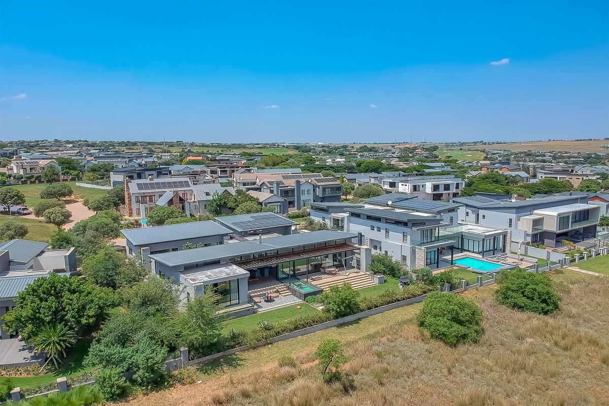 Aerial view of a modern residential property featuring a swimming pool, patio, landscaped garden, and solar panels within a well-maintained estate.