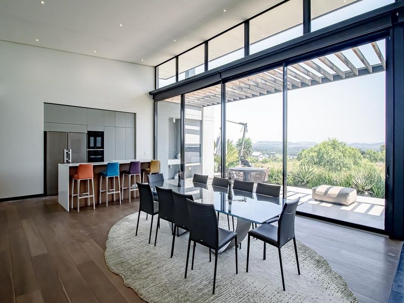 Spacious open-plan living and dining area featuring modern kitchen cabinetry, hardwood floors, and expansive floor-to-ceiling glass doors opening to an outdoor patio.