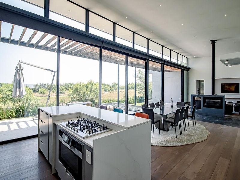 Modern open-plan living and kitchen area featuring a central island with gas cooktop, floor-to-ceiling glass doors, and a sleek fireplace.