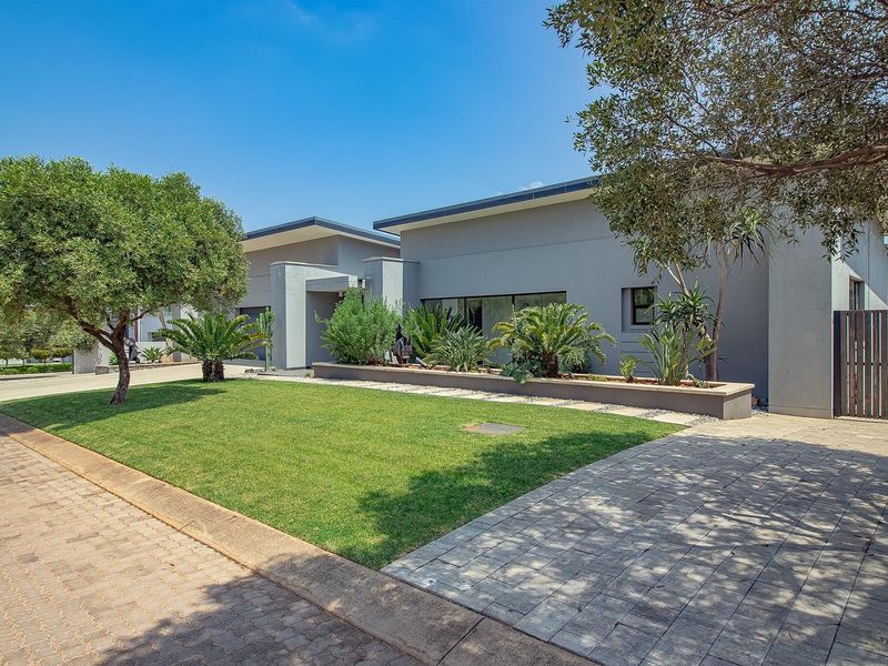 A modern, well-maintained front exterior featuring a paved driveway, manicured lawn, and landscaped garden beds against a contemporary grey facade.