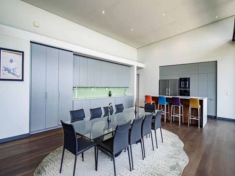 Modern open-plan kitchen and dining area featuring sleek grey cabinetry, integrated appliances, a central island, and high-quality hardwood flooring.