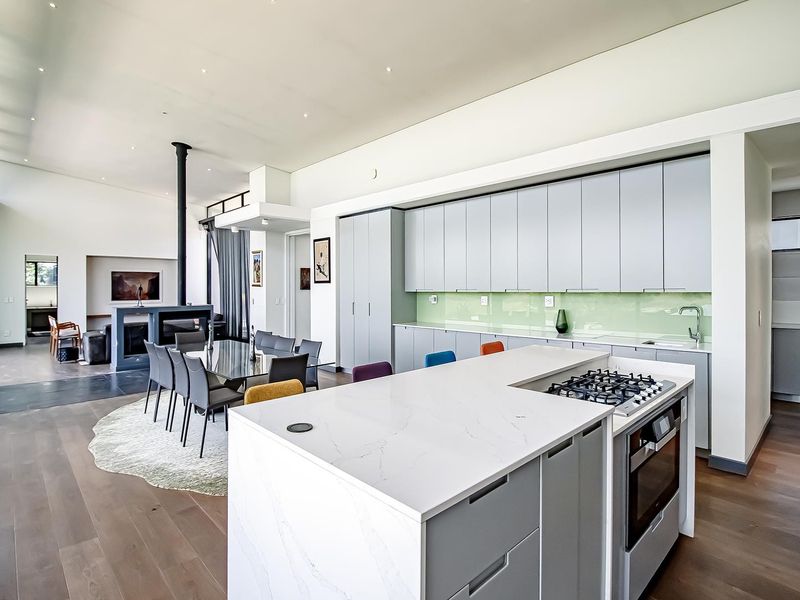 Modern open-plan living area featuring a sleek kitchen with stone island, gas cooktop, and a contemporary fireplace, seamlessly flowing into the dining space.