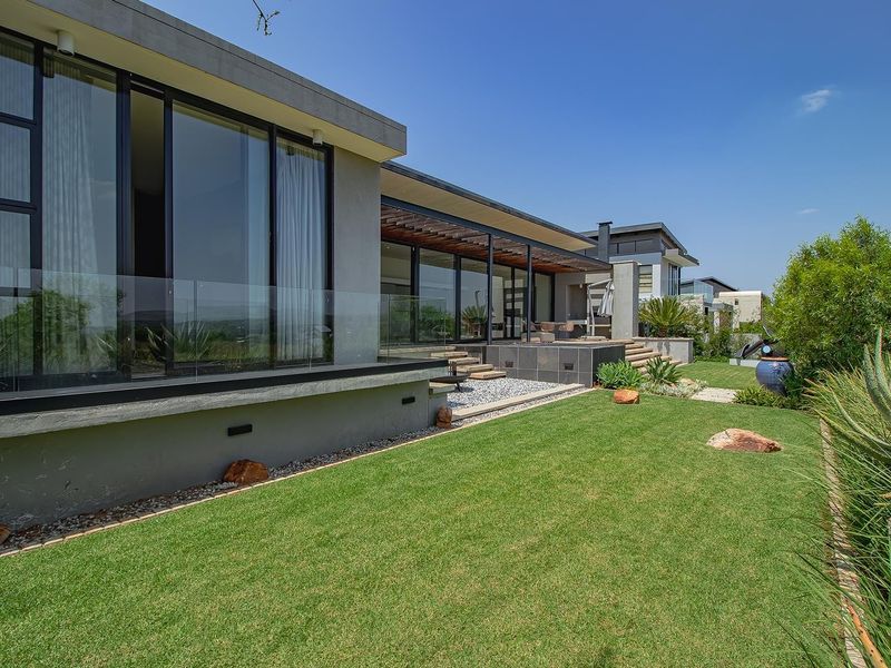 Modern rear elevation featuring expansive sliding glass doors, a covered patio with timber pergola, glass balustrades, and a well-maintained landscaped garden.