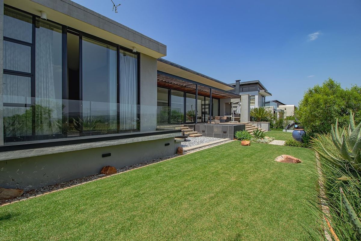 Modern rear elevation featuring expansive sliding glass doors, a covered patio with timber pergola, glass balustrades, and a well-maintained landscaped garden.