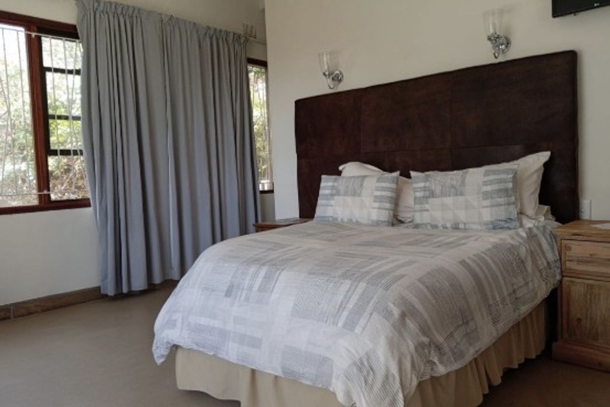A bedroom featuring a large built-in headboard and wall-mounted lighting fixtures, with neutral tones and window curtains.