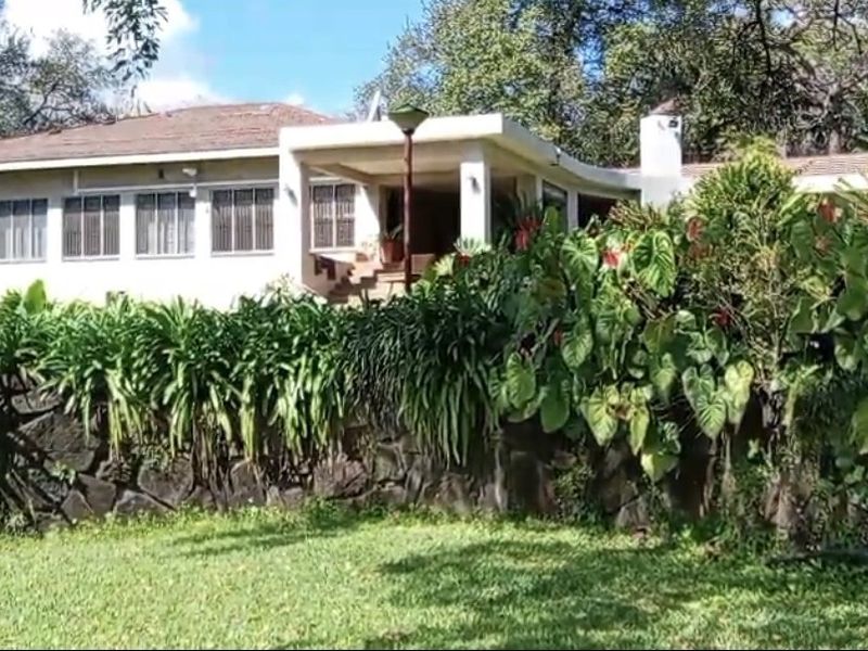 Rear view of a farm-style residence featuring a covered patio, stone retaining wall, and established garden landscaping.