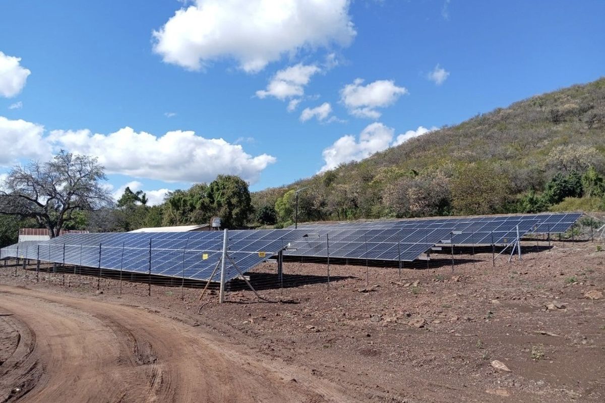 A large ground-mounted solar panel array installation situated on a rural farm property with dirt access road and hillside backdrop.