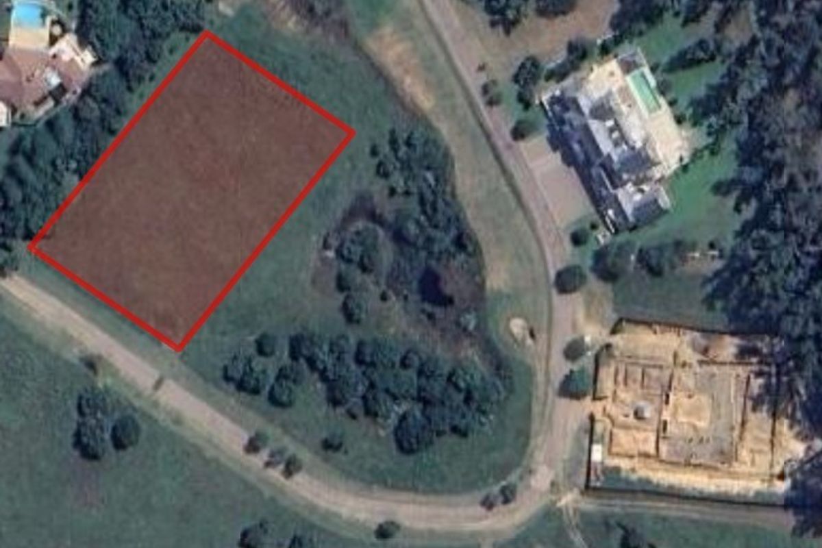 Aerial view of a vacant commercial land plot highlighted in red, situated within a developed residential or estate area.