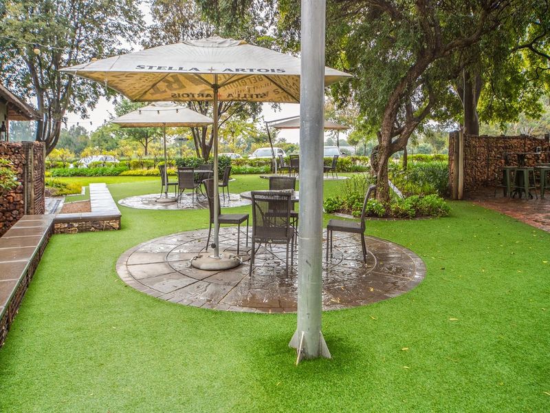 A well-maintained outdoor garden area featuring artificial turf, stone retaining walls, and paved circular seating sections under mature trees.