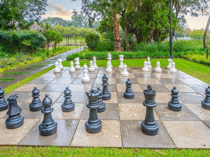 A well-maintained outdoor garden area featuring a large, permanent paved chess board set within a landscaped green space.