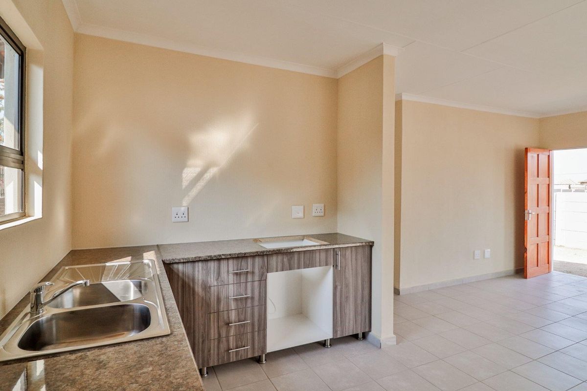 A functional kitchen area featuring modern cabinetry, a double stainless steel sink, granite countertops, and tiled flooring, leading into an open-plan living space.