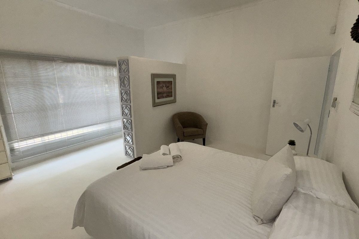 A bright bedroom featuring a decorative breeze block partition wall, neutral flooring, and large windows with fitted blinds.