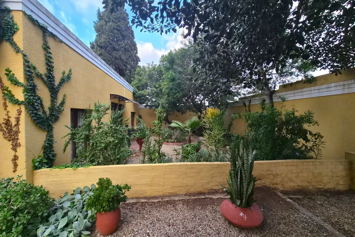 A private rear garden featuring a low brick boundary wall, established landscaping, and gravel pathways adjacent to the yellow-painted exterior of the house.