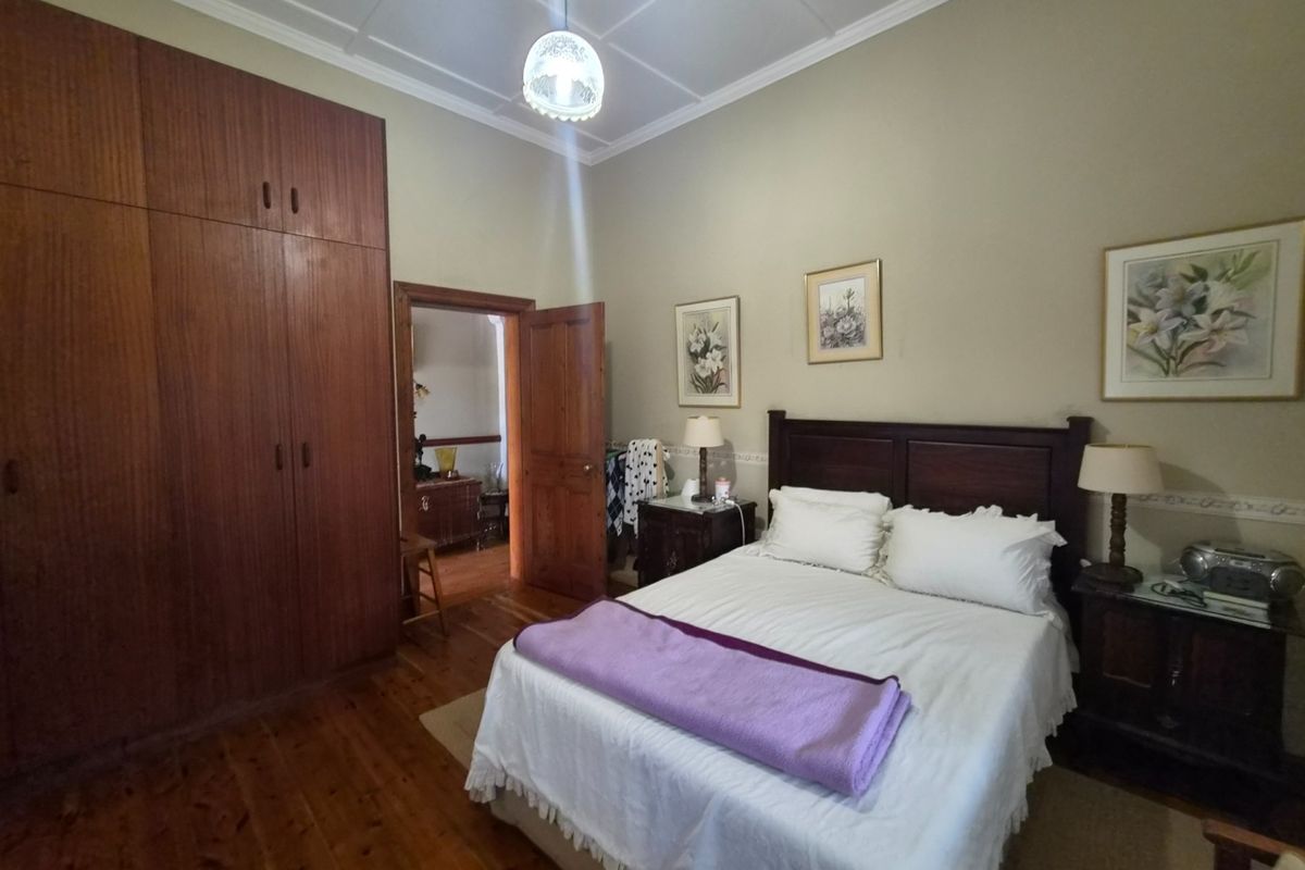 A spacious bedroom featuring polished timber flooring, high ceilings with decorative cornicing, and extensive built-in wooden cabinetry.
