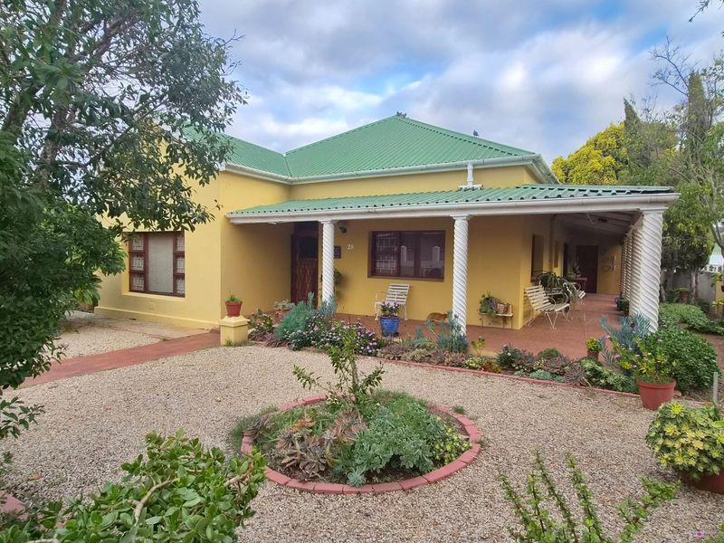 A charming single-story house featuring a green metal roof, yellow exterior walls, and a covered front veranda supported by decorative columns.