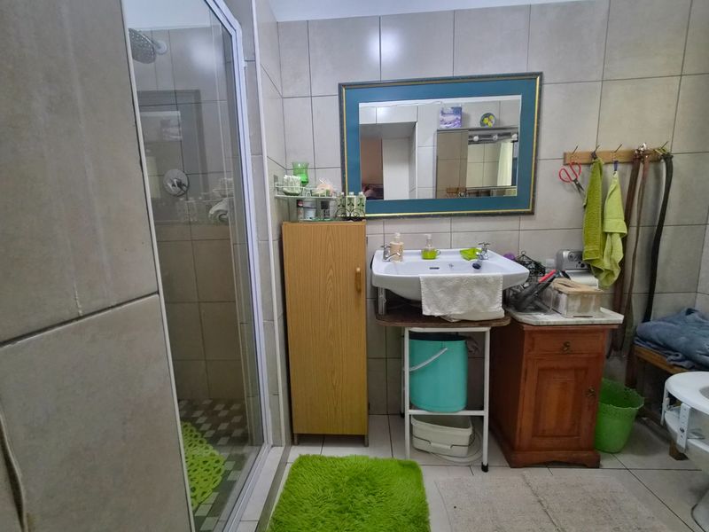 A functional bathroom featuring a glass-enclosed shower, wall-mounted basin, and tiled walls, offering a practical layout for daily use.