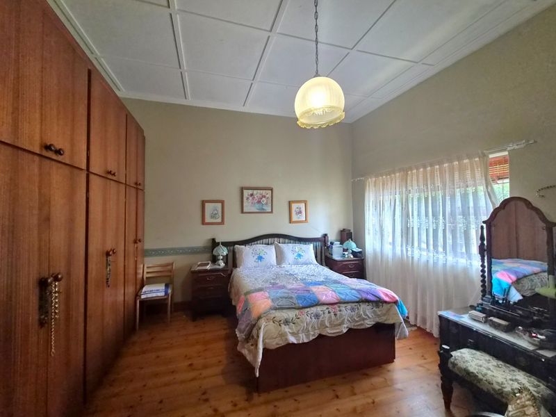 A spacious bedroom featuring built-in timber cabinetry, polished wooden flooring, and a classic pendant light fixture.