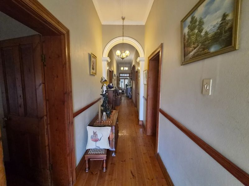 A long interior hallway featuring polished timber flooring, decorative archway, and classic wooden door frames connecting various rooms.