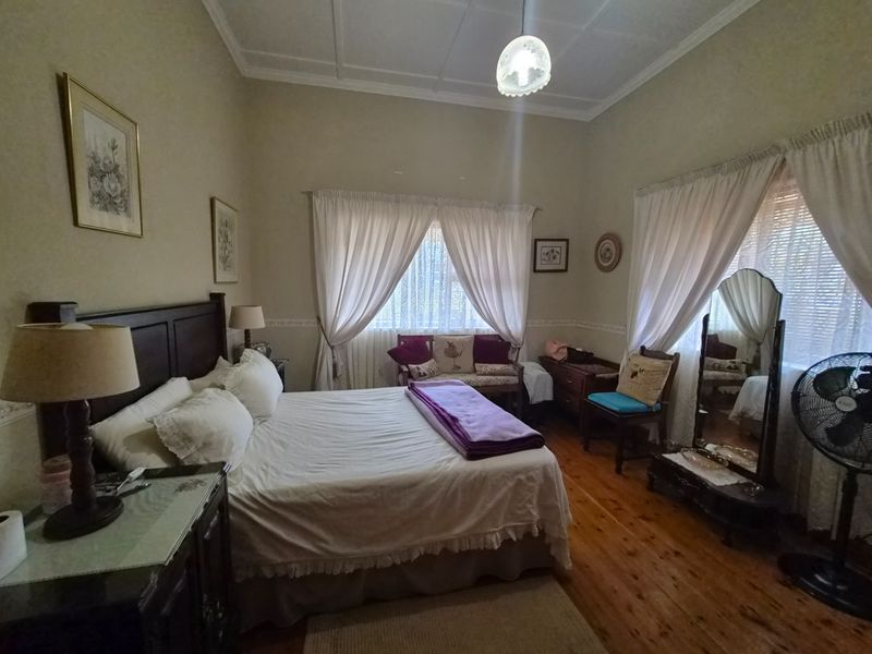 A spacious bedroom featuring original timber flooring, high ceilings with decorative cornicing, and dual windows with classic drapery.