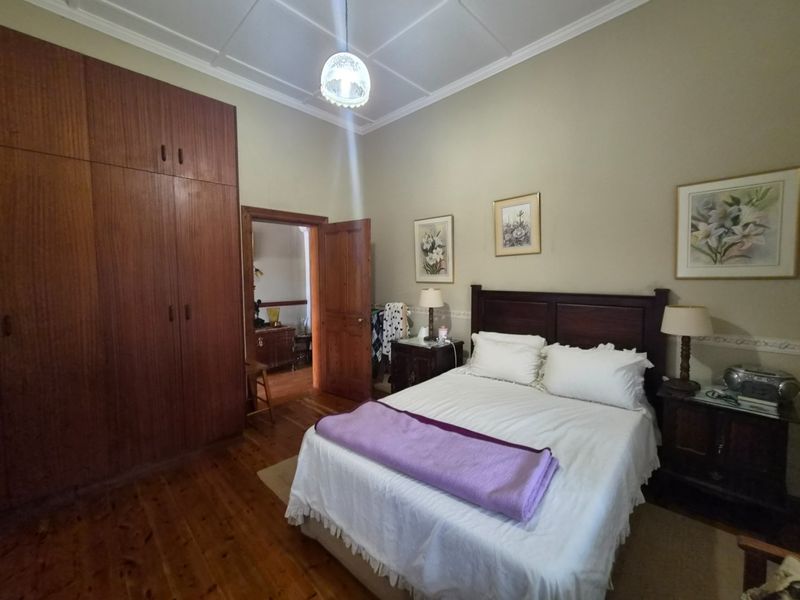 A spacious bedroom featuring polished timber flooring, high ceilings with decorative cornicing, and extensive built-in wooden cabinetry.