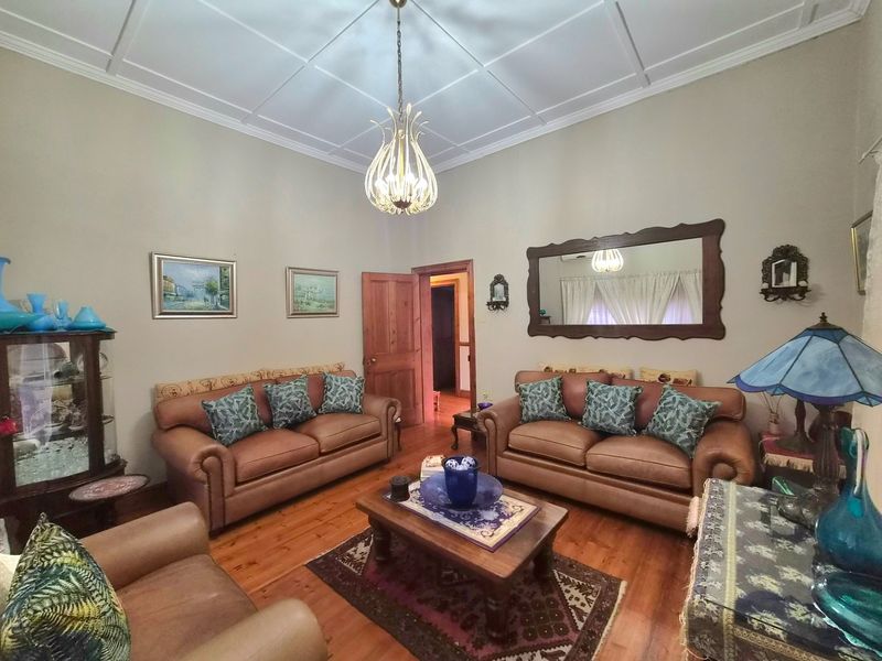 A traditional living room featuring polished timber flooring, high ceilings with decorative molding, and a classic chandelier, creating a warm and inviting atmosphere.