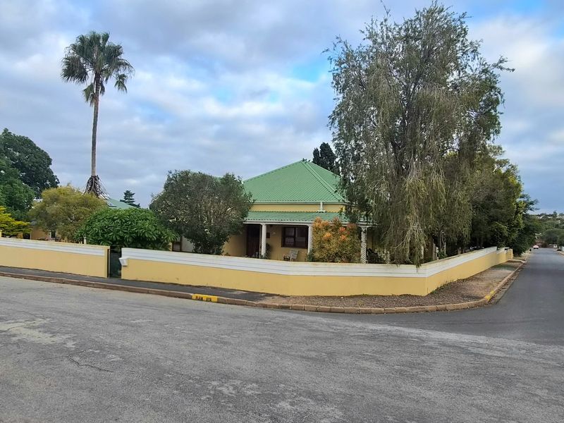 A corner-lot residential property featuring a green metal roof, a wrap-around veranda, and a perimeter boundary wall.