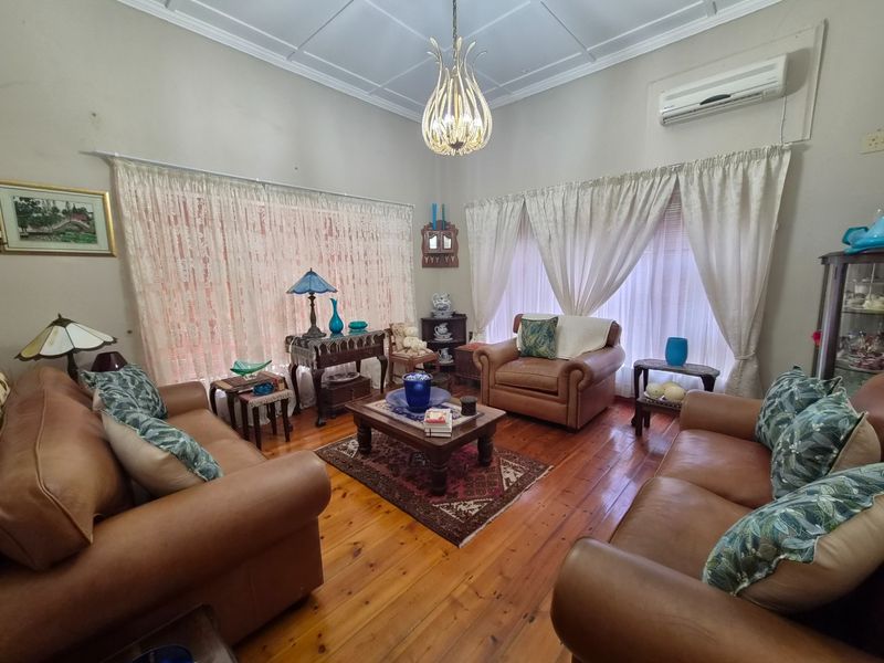 A traditional living room featuring polished timber flooring, high ceilings with decorative molding, and a wall-mounted air conditioning unit.