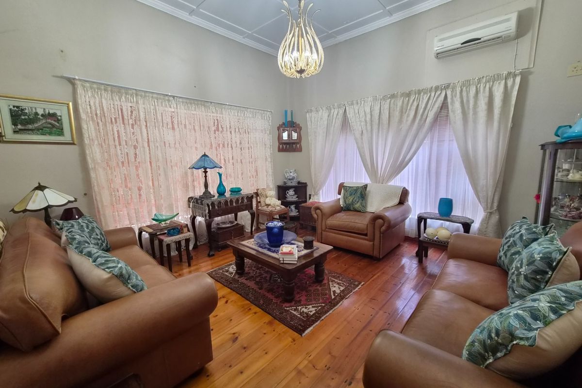 A traditional living room featuring polished timber flooring, high ceilings with decorative molding, and a wall-mounted air conditioning unit.