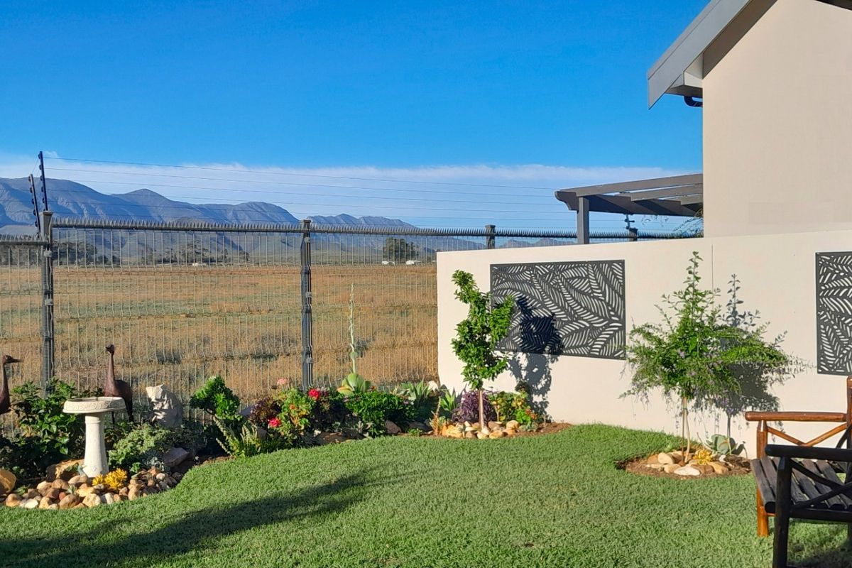 A well-maintained rear garden featuring a manicured lawn, decorative wall panels, and scenic mountain views, enclosed by secure perimeter fencing.