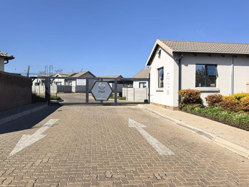 Secure gated entrance to the townhouse complex featuring paved driveway, security guard house, and perimeter fencing.