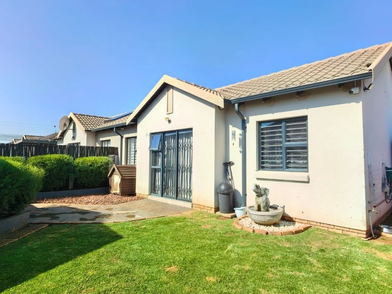 A well-maintained rear exterior view of the townhouse featuring a private garden, paved patio area, and secure sliding door access.